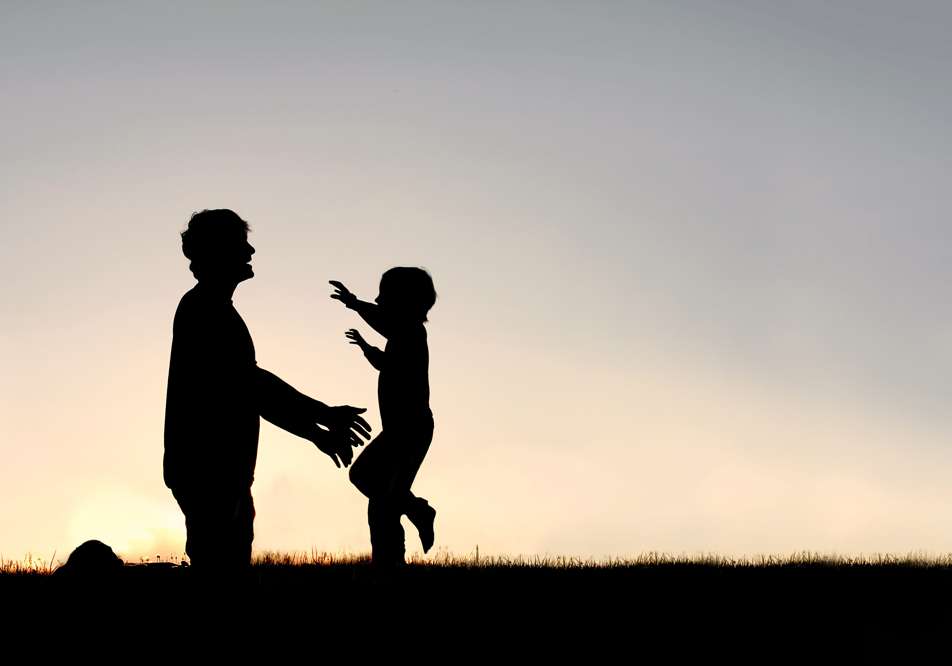 Silhouette of a happy young child smiling as he runs to greet his father with a hug at sunset on a summer day.